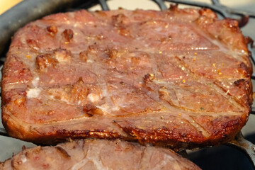 Turkey burger with grill marks while cooking above a fire pit on a sunny day of June 20, 2021. Below the grill surface, the fire consists mainly of mesquite dried-wood logs and fruit wood charcoal.