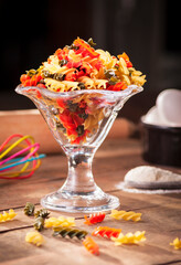 frontal view of a crystal goblet with colored fusilli pasta on a rustic wooden table