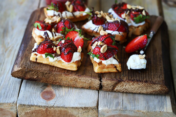 Waffles with fresh strawberries, cream cheese and chocolate on a wooden board. Healthy summer dessert.