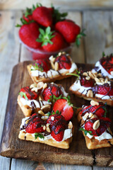 Waffles with fresh strawberries, cream cheese and chocolate on a wooden board. Healthy summer dessert.