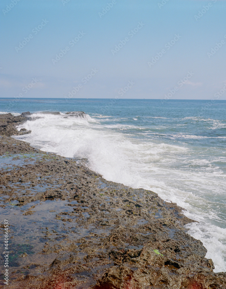 Wall mural vertical shot of a seascape with foamy coast under a blue clear sky