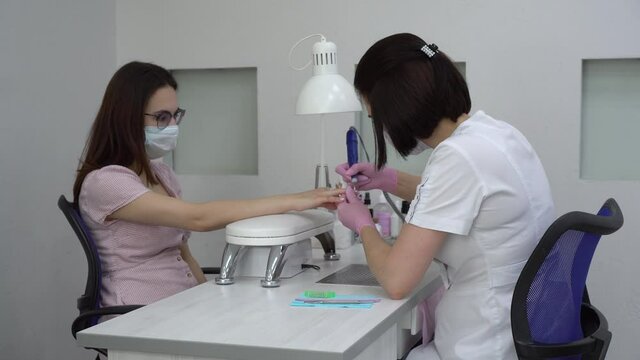 Young Asian woman with glasses in a manicure salon. A manicurist uses a drill machine to remove nails. The camera moves away.