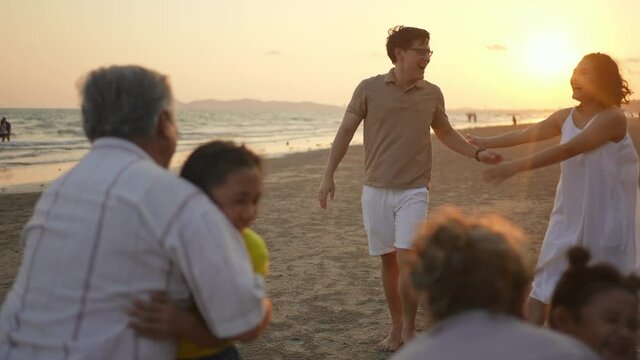 Happy multi-generation Asian family enjoy and having fun outdoor lifestyle activity together on the beach at summer sunset. Grandparents embracing two adorable grandchild girl sibling with happiness