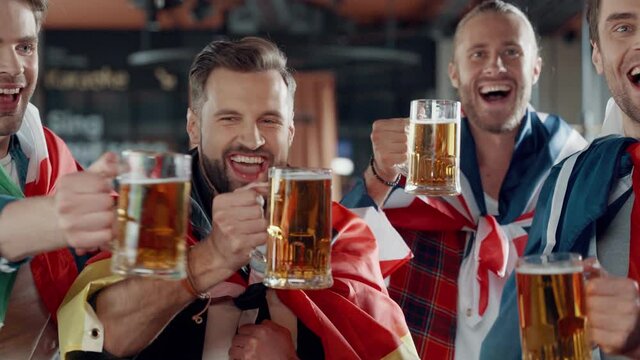 Happy young men covered in international flags toasting with beer 
