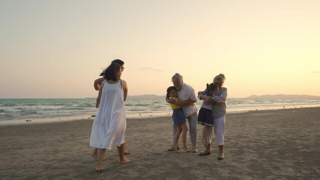 Happy multi-generation Asian family enjoy and having fun outdoor lifestyle activity together on the beach at summer sunset. Grandparents embracing two adorable grandchild girl sibling with happiness