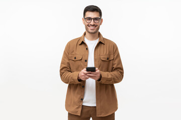 Smiling young man in casual brown shirt and glasses, holding smartphone, isolated on gray background