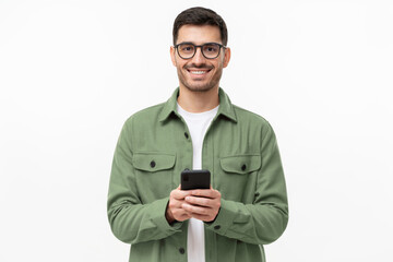 Young modern man in casual green shirt and glasses, holding smart phone in hands, looking at camera...