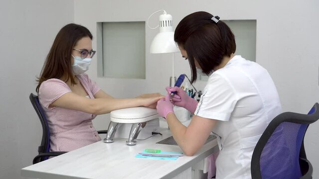 Young woman with glasses in a manicure salon. A manicurist uses a drill machine to remove nails.