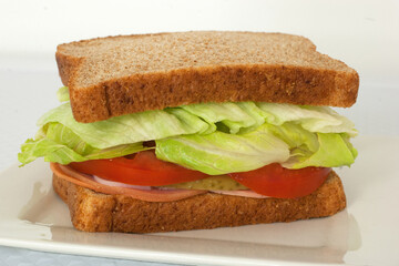 whole grain sub style cold cuts sandwich with sliced ham pepperoni and salami topped with cheese tomato lettuce pickle olives