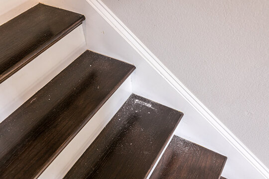 white painted and dark stained wood stairs in a new construction home with sheetrock dust from hole in the wall above