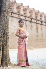 Portrait of an Asian female student dressed in traditional Thai clothes standing on the edge of the old city wall.