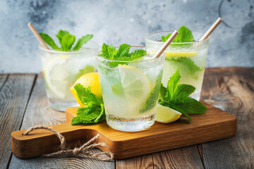 Two glass with lemonade or mojito cocktail with lemon and mint, cold refreshing drink or beverage with ice on rustic blue background