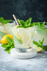 Two glass with lemonade or mojito cocktail with lemon and mint, cold refreshing drink or beverage with ice on rustic blue background