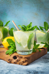 Two glass with lemonade or mojito cocktail with lemon and mint, cold refreshing drink or beverage with ice on rustic blue background. Copy space