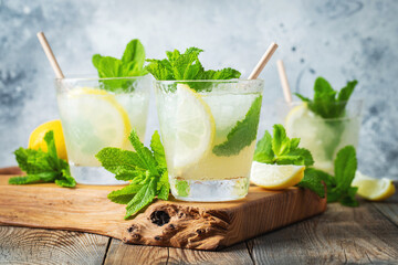 Two glass with lemonade or mojito cocktail with lemon and mint, cold refreshing drink or beverage with ice on rustic blue background