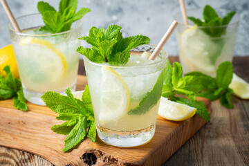 Two glass with lemonade or mojito cocktail with lemon and mint, cold refreshing drink or beverage with ice on rustic blue background