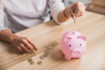 Young woman putting a coin inside piggy bank as savings for investment. Woman hand put coin money to piggy bank, saving and deposit money concept. Banking, economy concept.