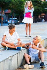 Two cheerful positive boys talking outdoors oblivious to offended girl