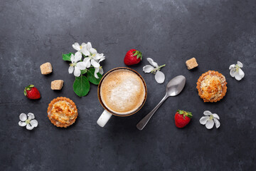 Cup of coffee with cakes and spring flowers on dark stone background. Top view