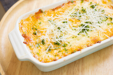 Close up and selective focus baked cheesy italian classic homemade food,lasagna with topping of vegetable and parmesan cheese served in wooden plate looks delicious menu for dinner or lunch.