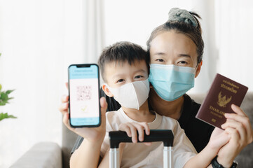 Asian mother and son wearing a face mask, is holding a passport and a smart phone with an example...