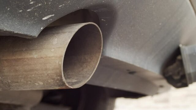 Detail shot looking into the exhaust pipe of a car, showing the vibration of the vehicle as the driver gets in and starts the engine.