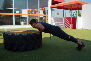 latin or native american men doing push ups in a tire outdoors in front of his gym in a sunny day