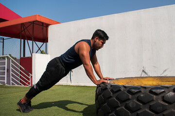 latin or native american men doing push ups in a tire outdoors in front of his gym in a sunny day
