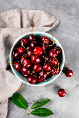 A bowl ripe cherries on a light gray background top view, summer berries on the table vertical photo