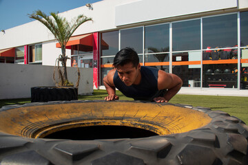 latin or native american men doing push ups in a tire outdoors in front of his gym in a sunny day