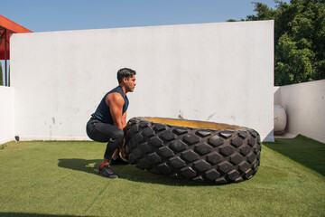 latin or native american man lifting up a tire while he´s doing crossfit outside of his gym in a sunny day