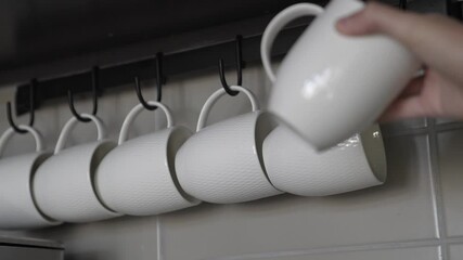 This POV video shows a hand taking a coffee cup off of a rack of lined with white mugs.