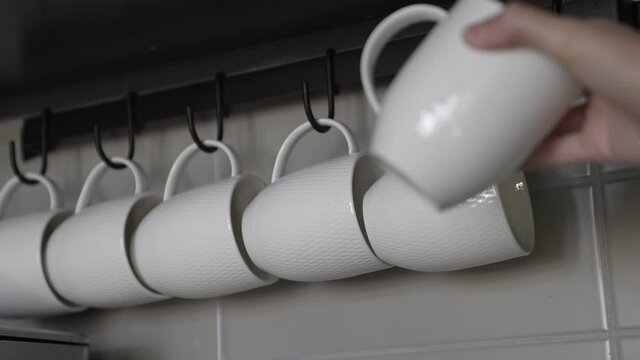 This POV video shows a hand taking a coffee cup off of a rack of lined with white mugs.