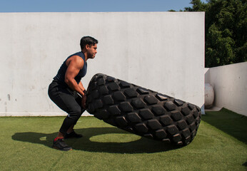 latin or native american man lifting up a tire while he´s doing crossfit outside of his gym in a...