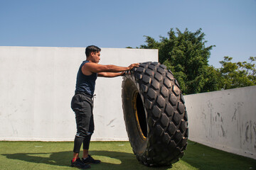 latin or native american man lifting up a tire while he´s doing crossfit outside of his gym in a sunny day