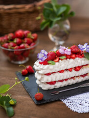 Pavlova dessert with strawberries and violet flowers as a decor on a wooden background