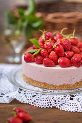 Strawberry cheesecake with a decor of a large number of strawberries lying on a lace napkin on a wooden background