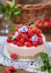 Strawberry cheesecake with a decor of a large number of strawberries and violet flowers lying on a lace napkin on a wooden background