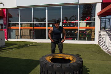 latin or native american man lifting up a tire while he´s doing crossfit outside of his gym in a sunny day