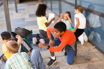 Smiling friendly preteen schoolmates funning outside near school during break between lessons in sunny spring day.