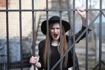 A girl walks down the city street in a leather waistcoat with a phone. Young beautiful girl in a hat and with a dark make-up outside. Girl in the Gothic style on street.