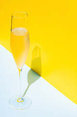 A glass of cold Champagne with vapour that has shadow from sun light on blue and yellow background. Summer concept.