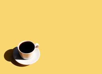 Cup and plate of coffee with shadow of sun on yellow beige terracotta background