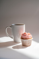 A cupcake or muffin stands next to a cup of coffee.