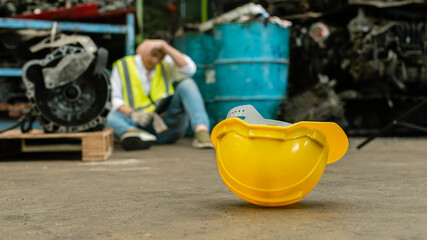 Close up yellow safety hardhat on floor with man stressed and unemployed in factory, standard horizontal banner 16:9. - obrazy, fototapety, plakaty