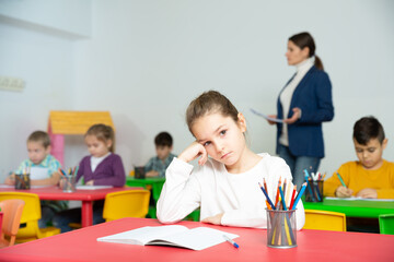 Sad bored schoolgirl sitting separately in classroom during lesson in elementary school