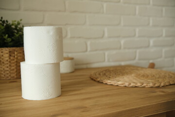 Toilet paper on a wooden table. Two white rolls. Brick background. A green flower. White and beige colors