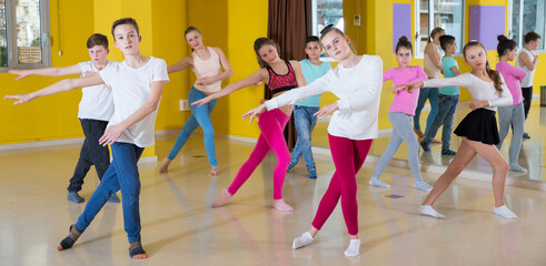 Children dancing synchronous group choreography with female coach in dance hall