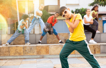 Confident tween boy hip hop dancer posing while performing with group on summer city street.