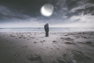 Scary view of a hand rising out of beach sand under full moon